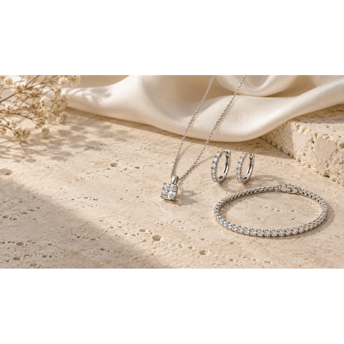 Cushion-cut moissanite pendant necklace, silver pavé hoop earrings and a moissanite tennis bracelet arranged on ivory travertine.
