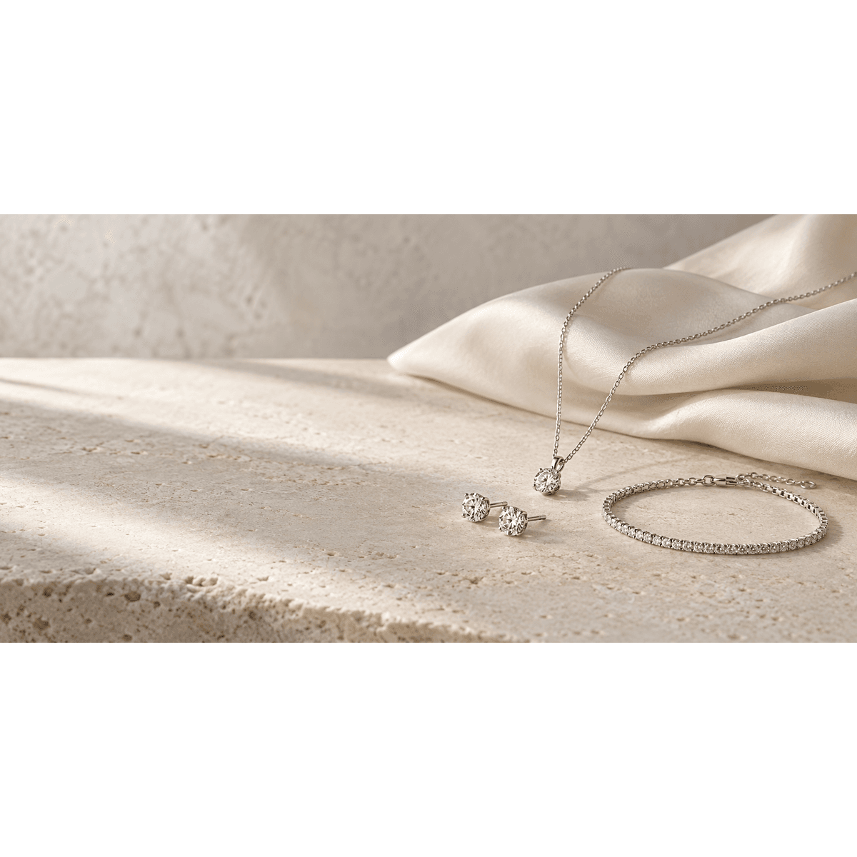 Delicate moissanite necklace, stud earrings and silver bracelet styled on ivory stone and cream silk